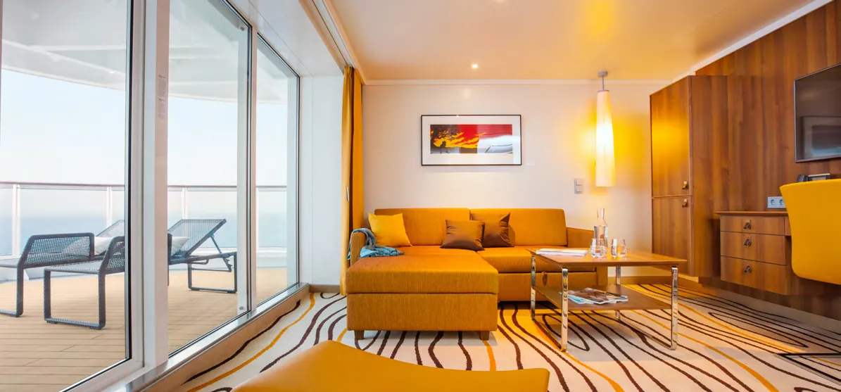 Moderne AIDA Suite mit gemütlicher Sitzecke, großem Balkon und Meerblick – stilvoller Wohnkomfort für anspruchsvolle Kreuzfahrtgäste.