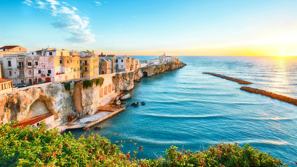 Blick auf die malerische Altstadt von Vieste in Apulien, Süditalien, mit historischen Häusern auf steilen Klippen über dem türkisblauen Meer bei Sonnenuntergang.