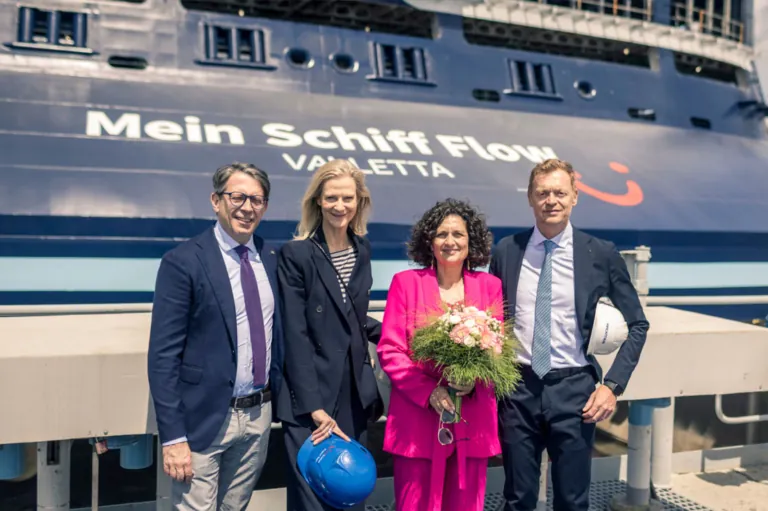 Vier Personen in festlicher Kleidung posieren vor dem Kreuzfahrtschiff "Mein Schiff Flow" in Valletta; eine Frau in Pink hält einen Blumenstrauß.