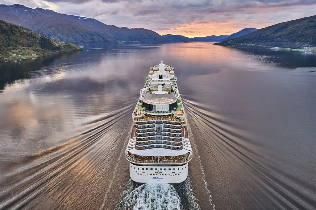Das Kreuzfahrtschiff AIDAnova fährt durch einen ruhigen Fjord bei Sonnenuntergang.