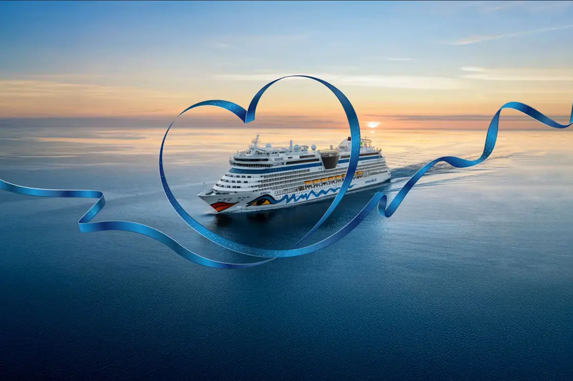 Kreuzfahrtschiff AIDAluna auf dem Meer bei Sonnenuntergang, eingerahmt von einem großen, blauen Herzband.