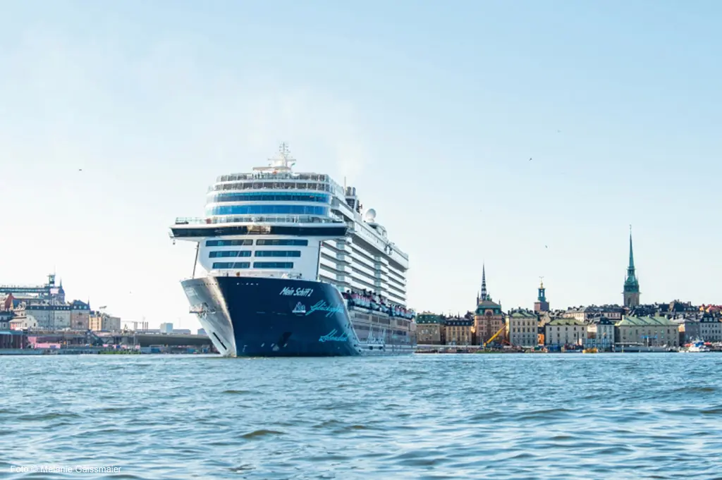 Kreuzfahrtschiff „Mein Schiff“ fährt in den Hafen von Stockholm ein, im Hintergrund die Skyline mit Kirchen und historischen Gebäuden.
