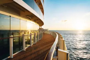 Sonnenuntergang über dem Meer, gesehen vom Außendeck eines Kreuzfahrtschiffs mit Glasgeländer.