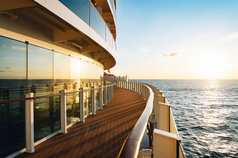 Sonnenuntergang über dem Meer, gesehen vom Außendeck eines Kreuzfahrtschiffs mit Glasgeländer.