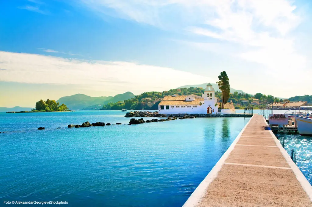 Blick auf das Kloster Vlacherna auf Korfu, Griechenland, umgeben vom türkisblauen Meer und sanften Hügeln im Hintergrund.