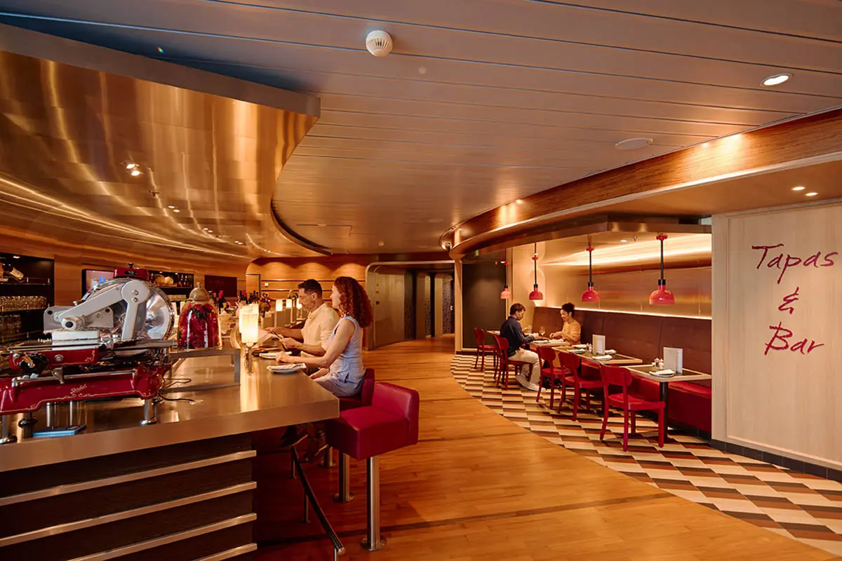 Tapas & Bar Bereich auf der AIDAbella mit Bartresen, roten Stühlen und gemütlicher Sitzatmosphäre.