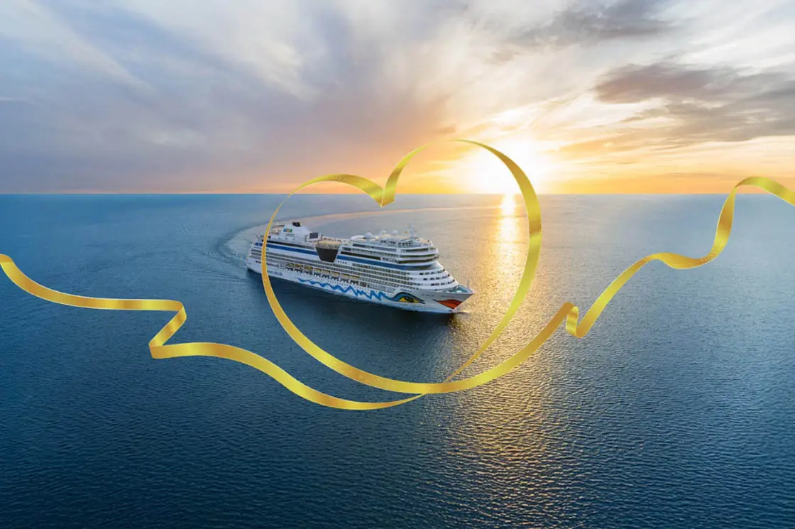 AIDA Kreuzfahrtschiff fährt bei Sonnenuntergang über das Meer, umrahmt von einer goldenen Herzgrafik.