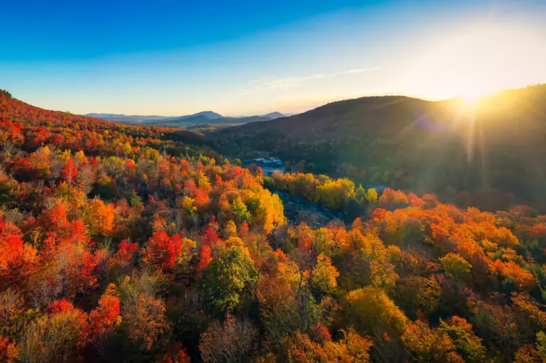 Indian Summer in Neuengland mit leuchtend roten, orangefarbenen und gelben Herbstwäldern, sanften Hügeln und tief stehender Sonne.